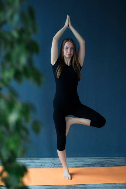 mujer joven haciendo pose de árbol, vrikshasana pose en esterilla de yoga y relajarse respirando en el estudio. - brain gym fotografías e imágenes de stock