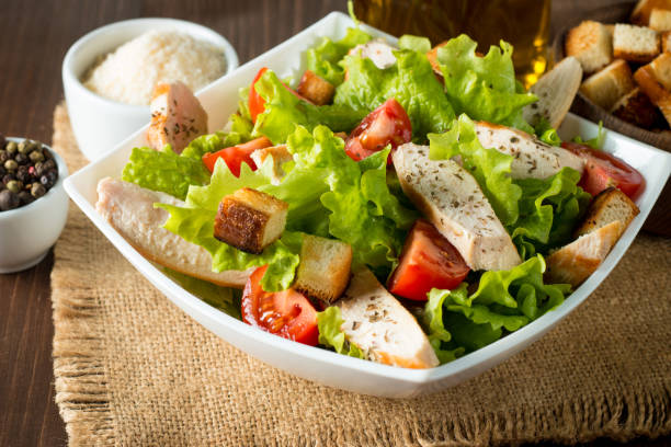 Fresh salad made of tomato, ruccola, chicken breast, eggs, arugula, crackers and spices. Caesar salad in a white, transparent bowl on wooden background Fresh salad made of tomato, ruccola, chicken breast, eggs, arugula, crackers and spices. Caesar salad in a white, transparent bowl on wooden background salad fruit lettuce spring stock pictures, royalty-free photos & images