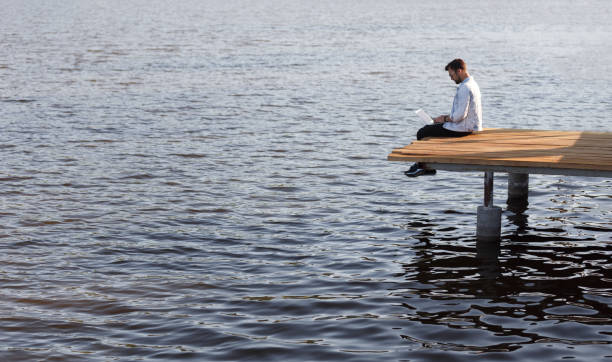 istock Man using laptop on pier above calm water 1148231362