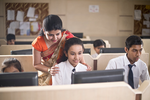 Teacher assisting a school girl in computer class