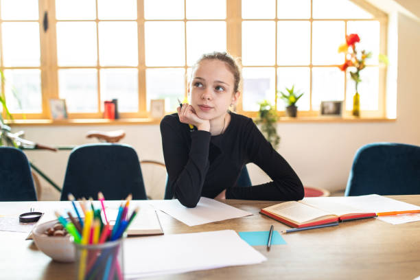 Thoughtful female teenage student in classroom Thoughtful female teenage student leaning on desk, looking away, at classroom in school boring homework twelve stock pictures, royalty-free photos & images