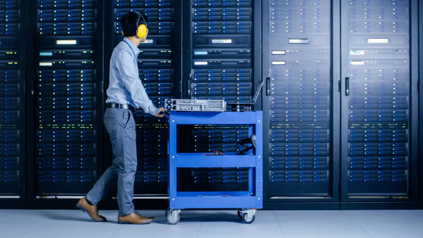istock In the Modern Data Center: IT Engineer Doing Maintenance and Diagnostics. Pushes Cart alongside Server Racks, Opens Cabinet to Install New Hardware for Planned System Update, Equipment Replacement. 1148233797