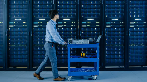 istock In the Modern Data Center: IT Engineer Pushes Cart alongside Server Racks and Cabinets to Install New Hardware for Planned System Update, Equipment Replacement. 1148233821