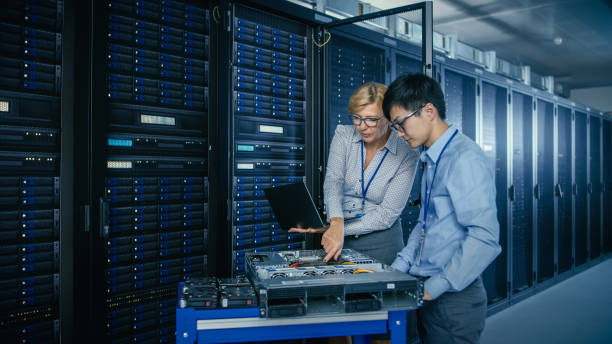 istock In the Modern Data Center: Engineer and IT Specialist Work with Server Racks, on a Pushcart Equipment for Installing New Hardware. Specialists Doing Maintenance and Diagnostics of the Database. 1148233823