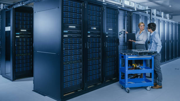 istock In the Modern Data Center: Engineer and IT Specialist Work with Server Racks, on a Pushcart Equipment for Installing New Hardware. Specialists Doing Maintenance and Diagnostics of the Database. 1148233825