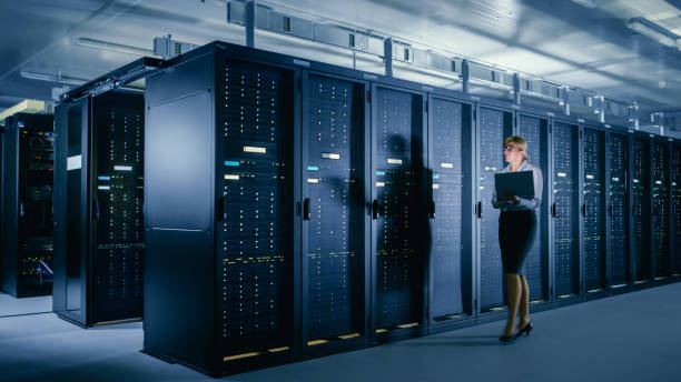 istock In Data Center: Female IT Technician Walks Alongside Row of Server Racks, Uses Laptop Computer to Run Maintenance Diagnostics so that Mainframe Works at Optimal Functioning Level. 1148233865