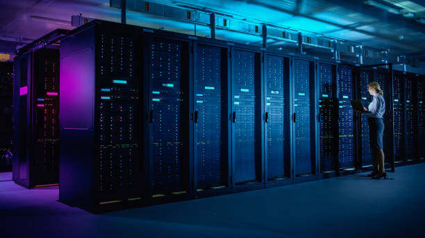 In Data Center: IT Technician Running Maintenance Programme on Laptop, Controls Operational Server Rack Optimal Functioning. Modern High-Tech Telecommunications Operational Data Center in Neon Lights. en el centro de datos: técnico de ti ejecutando el programa de mantenimiento en el portátil, controla el funcionamiento óptimo del bastidor del servidor operativo. moderno centro de datos operacionales de telecomunicaciones de alta tecnología en luces