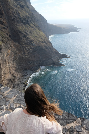 Woman with long hair looking to ocean cliffs from up above