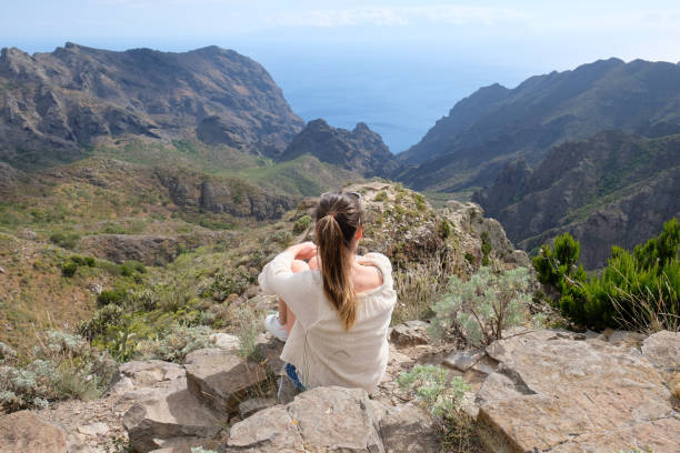 istock Girl sitting on a cliff looking to a valley 1148235668