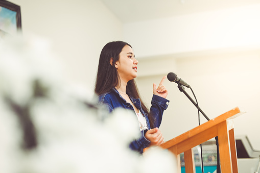 Pretty young lady, 18 years old, stands at a podium, maybe in school or at church and she gives a speech or perhaps she is singing. She is confident and accomplished looking. She is on the verge of something. She is mixed of, Asian, Thai and Latina ancestry