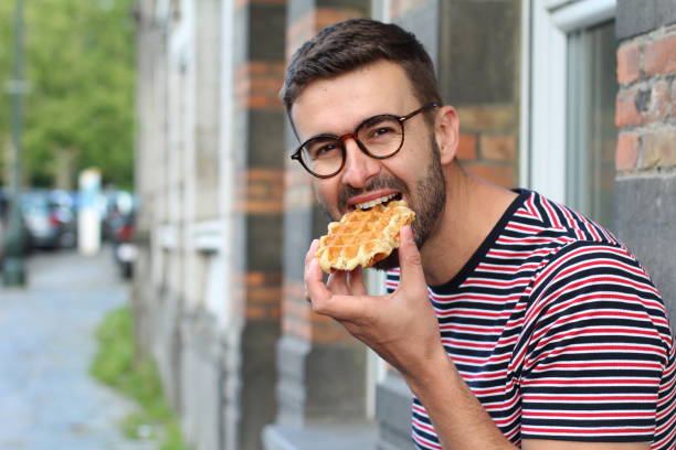 cute guy eating a waffle in brussels, belgium - brussels waffle belgian waffle people imagens e fotografias de stock