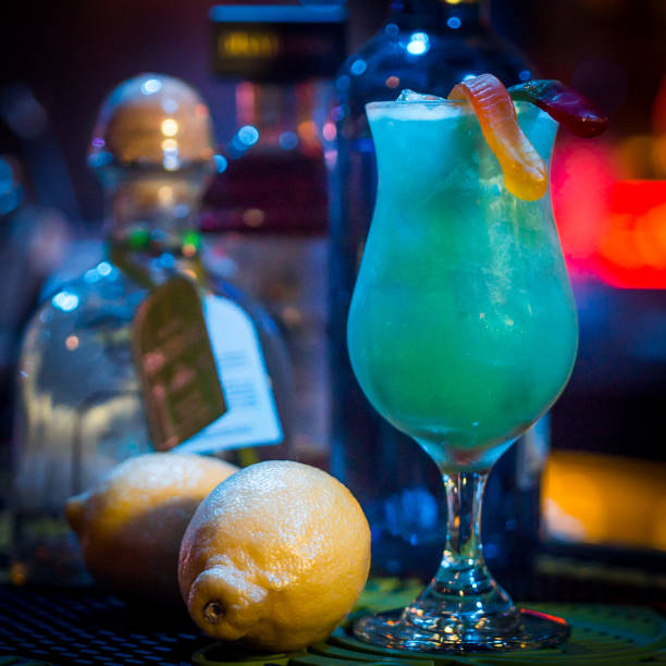 Gummy Worms Halloween Cocktail A spooky blue green Halloween cocktail garnished with gummy worms. Bottles of ingredients and lemons in the background. tequila worm stock pictures, royalty-free photos & images