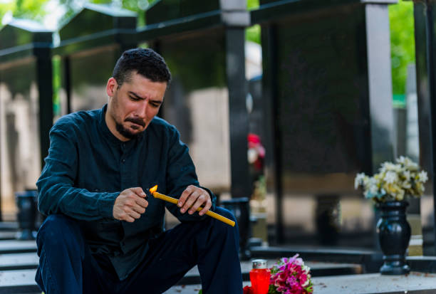 emotional gestresst mann mit einer kerze auf dem friedhof - spooky cemetery single flower flower stock-fotos und bilder