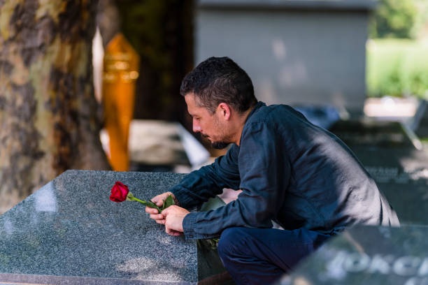 man platziert rote rosenblüte am grabstein auf friedhof - spooky cemetery single flower flower stock-fotos und bilder
