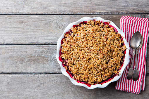 Berry crumble in white baking dish on grey wooden background. Top view. Copy space
