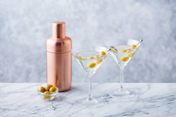 Martini cocktail with green olives, shaker on marble table background.