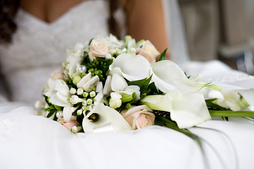 Buds of cream roses combined with white calla and freesia in a wedding bouquet on a blurred background of the bride