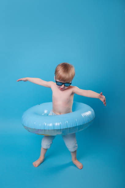 summer portrait of little boy with sunglasses and inflatable ring on blue background - swimming child swimwear little boys imagens e fotografias de stock