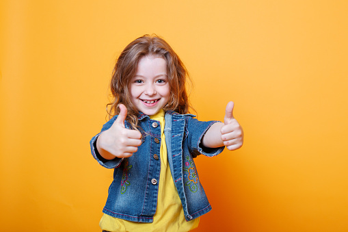 Stylish little girl showing thumbs up on orange background