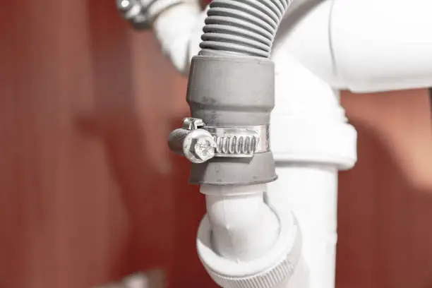 Photo of Metal clamp for connection of dishwasher drain hose under kitchen sink close up