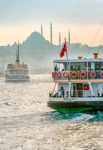 Istanbul, Turkey April 07, 2019: Muslim architecture and water transport in Turkey - Beautiful View touristic landmarks from sea voyage on Bosphorus. Cityscape of Istanbul at sunset - old mosque and turkish steamboats, view on Golden Horn.