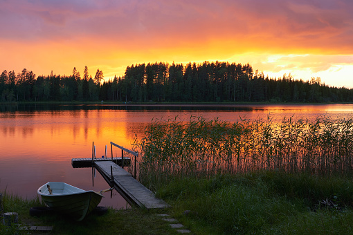 Summer sunset on the shore of a Finnish lake, with a small pier and a boat.