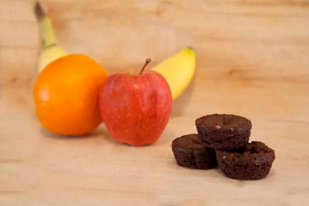 A small pile of brownies beside an apple, banana and orange make different dessert choices