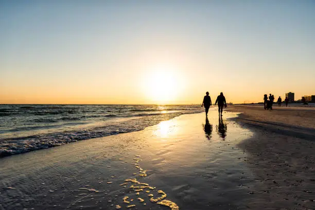 Photo of Sarasota, USA Sunset sun in Siesta Key, Florida with coastline ocean gulf of mexico on beach shore and many people couple silhouette walking by waves