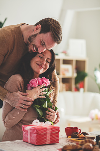 Romantic mid adult man cuddling his smiling girlfriend after giving her gift and bouquet of roses on a date.