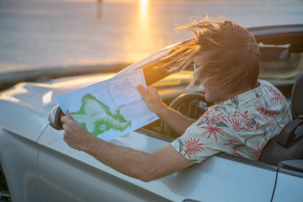 istock Young man inside convertible car looking at road map for directions at sunset 1148310216