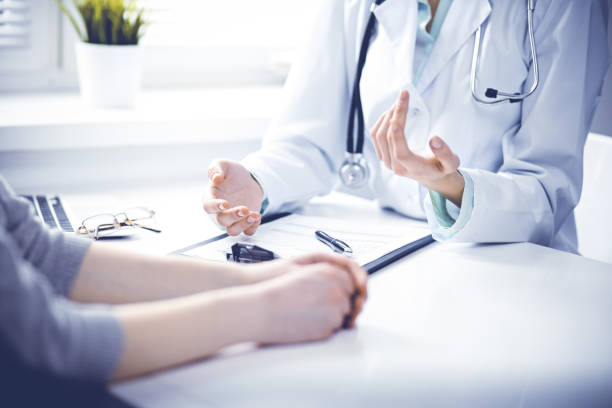 Doctor and female patient sitting at the desk and talking in clinic near window. Medicine and health care concept. Green is main color Close up of doctor and patient sitting at the desk near the window in hospital doctor general practitioner stock pictures, royalty-free photos & images