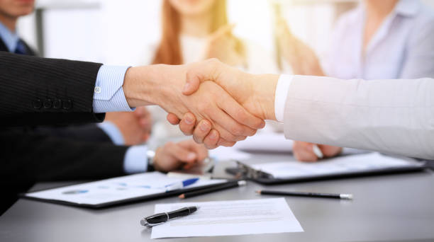 istock Business people shaking hands at meeting while theirs colleagues clapping and applauding. Group of unknown businessmen and women in modern white office. Success teamwork, partnership and handshake concept 1148335206