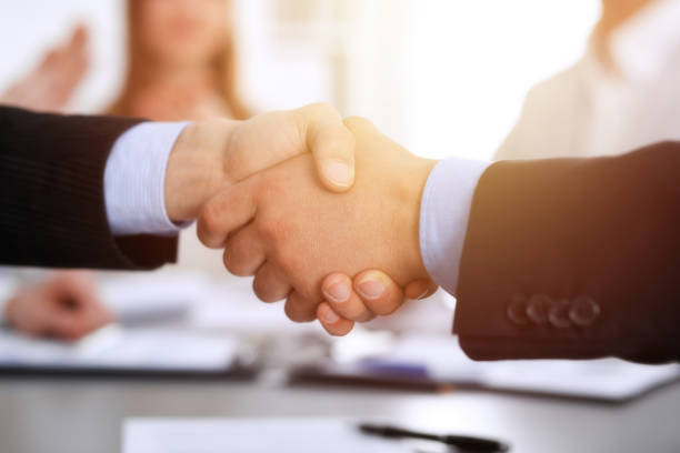 istock Business people shaking hands at meeting while theirs colleagues clapping and applauding. Group of unknown businessmen and women in modern white office. Success teamwork, partnership and handshake concept 1148335212