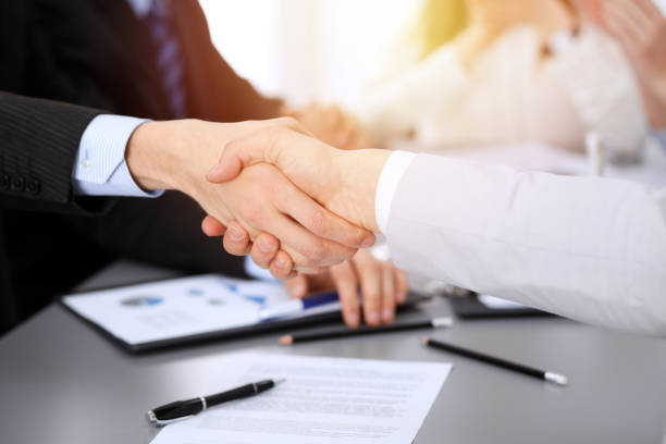 istock Business people shaking hands at meeting while theirs colleagues clapping and applauding. Group of unknown businessmen and women in modern white office. Success teamwork, partnership and handshake concept 1148335220