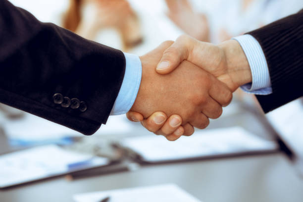 istock Business people shaking hands at meeting while theirs colleagues clapping and applauding. Group of unknown businessmen and women in modern white office. Success teamwork, partnership and handshake concept 1148336287
