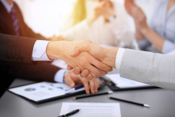 istock Business people shaking hands at meeting while theirs colleagues clapping and applauding. Group of unknown businessmen and women in modern white office. Success teamwork, partnership and handshake concept 1148337341