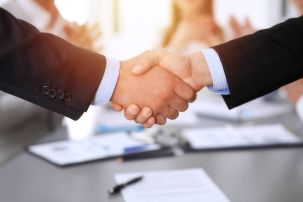 istock Business people shaking hands at meeting while theirs colleagues clapping and applauding. Group of unknown businessmen and women in modern white office. Success teamwork, partnership and handshake concept 1148337345