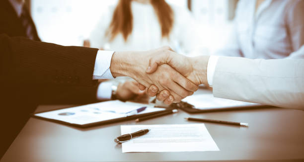 istock Business people shaking hands at meeting while theirs colleagues clapping and applauding. Group of unknown businessmen and women in modern white office. Success teamwork, partnership and handshake concept 1148338601
