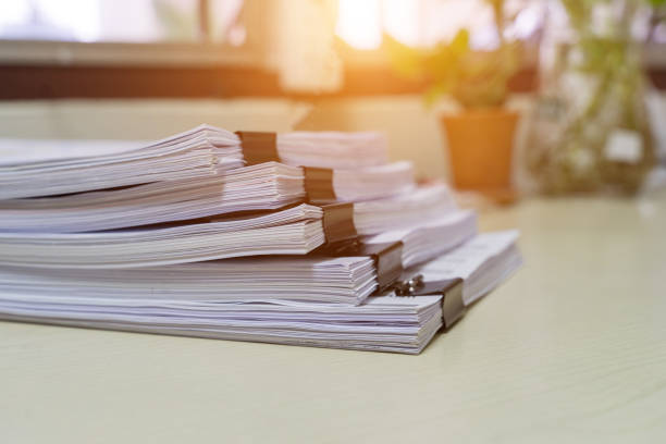 istock Education concept: Close and selective focus of unfinished homework assignment stack archives with binder paper clips on teacher’s desk in university waiting to be evaluated and scored. Stack of white paperwork achieves with black binder paper clips. Sta 1148343990