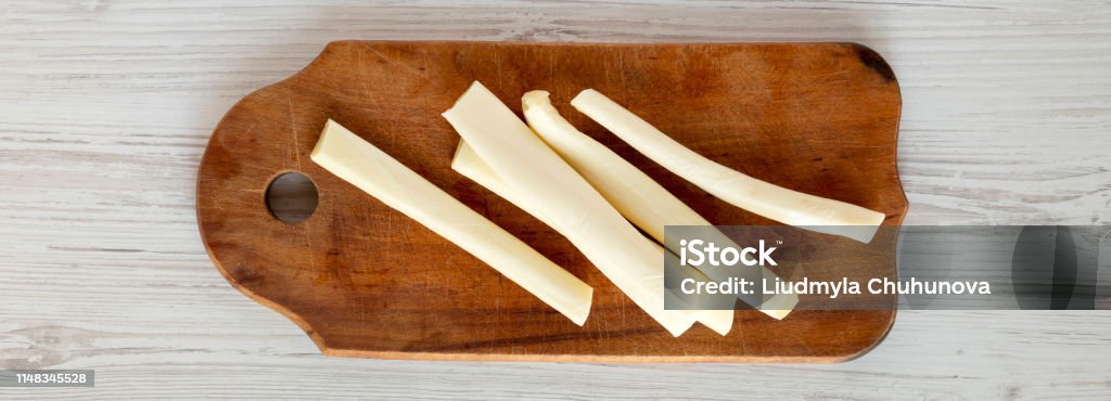 String cheese on rustic wooden board over white wooden background, top view. Healthy snack. From above, overhead, flat lay. String Cheese Stock Photo