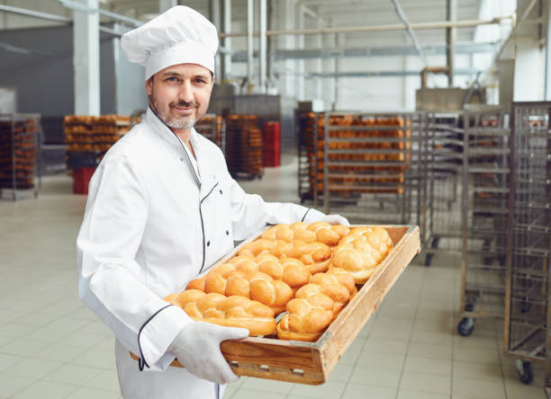 un panadero en una panadería contra las estanterías de pan. - food industry manufacturing human hand fotografías e imágenes de stock