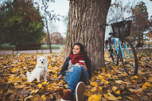 Relaxed girl with her dog drinking coffee in the park