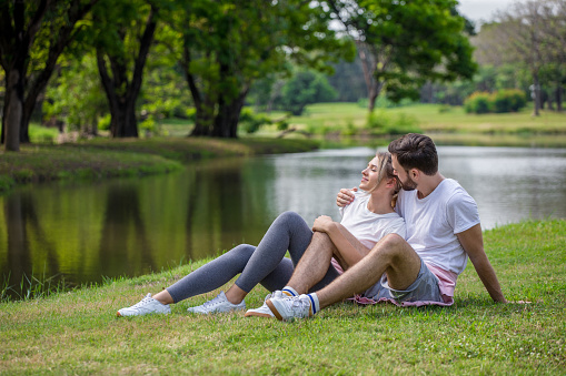Happy young couple loving fitness in sportswear relaxing at park together in morning time. sport people sitting taking a break after exercises. resting . relationships. training,workout
