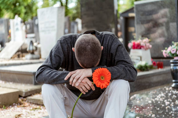 Man Placing Red Rose Flower at Tombstone In Cemetery