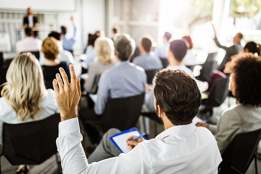 Vista trasera de un empresario levantando la mano en un seminario. photo