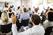 Back view of a businessman raising his hand on a seminar.