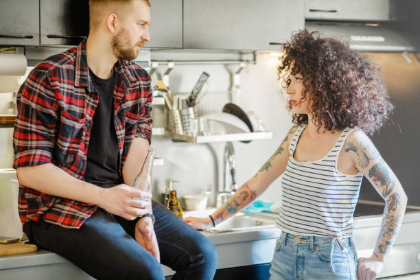 Young man talking seriously with his female flatmate Young man sitting on kitchen counter and having serious talk with his female flatmate flatmate stock pictures, royalty-free photos & images