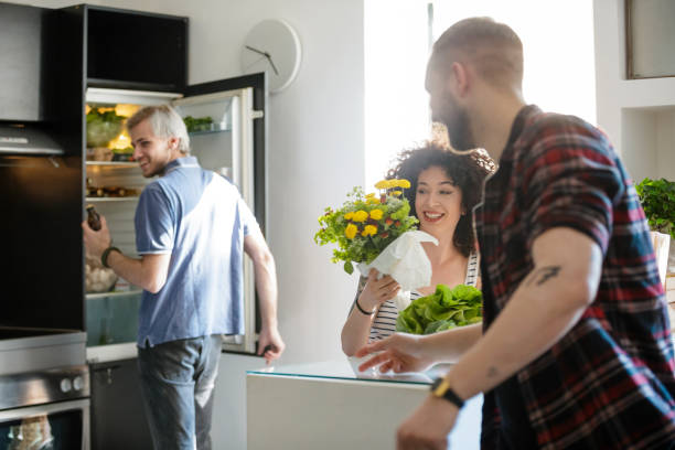 smiling young woman with flowers in the kitchen with flatmates - three different refrigerators imagens e fotografias de stock