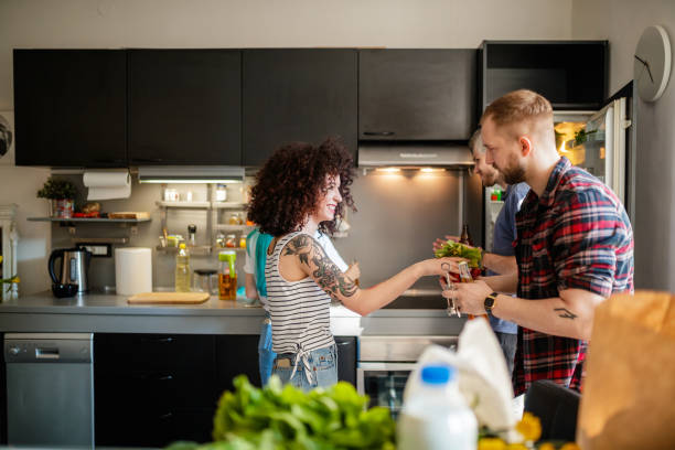 Young woman giving her flatmate a bunch of radish Young woman smiling and giving a bunch of radish to her flatmate holding beer bottle and opener flatmate stock pictures, royalty-free photos & images