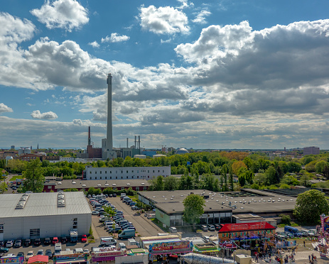Braunschweig, Germany, May 5., 2019: Aerial view of the caravans of the carnies standing behind the rides of a fairground. A combined heat and power plant with a long chimney in the back